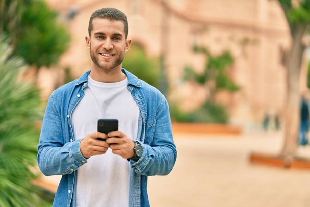 Jeune homme caucasien souriant heureux en utilisant un smartphone au parc. - Photo, image