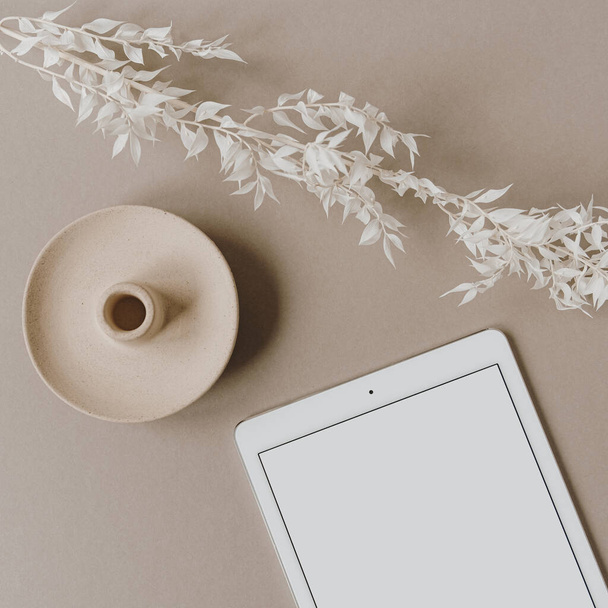 ブランクスクリーンタブレット、中性パステルベージュの背景に白い花の枝。フラットレイアウト、トップビューミニマリストライフスタイルブログ、ウェブサイトテンプレート。コピースペースモックアップ. - 写真・画像
