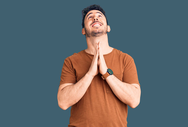 Jonge Latijns-Amerikaanse man in casual kleding bedelend en biddend met de handen samen met hoop uitdrukking op het gezicht zeer emotioneel en bezorgd. bedelen.  - Foto, afbeelding