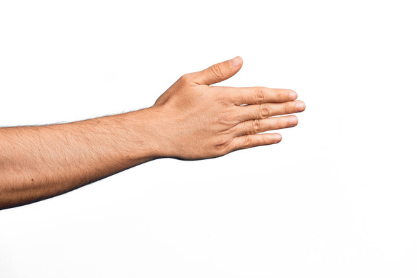 Mano de joven caucásico mostrando los dedos sobre fondo blanco aislado estirándose y alcanzando con la mano abierta para apretón de manos, mostrando la parte posterior de la mano - Foto, imagen