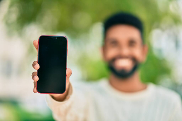 Joven afroamericano hombre sonriendo feliz mostrando la pantalla de teléfono inteligente en la ciudad. - Foto, Imagen