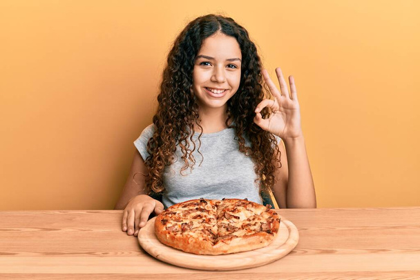 adolescent hispanique fille manger italien pizza faire ok signe avec les doigts, sourire geste amical excellent symbole  - Photo, image