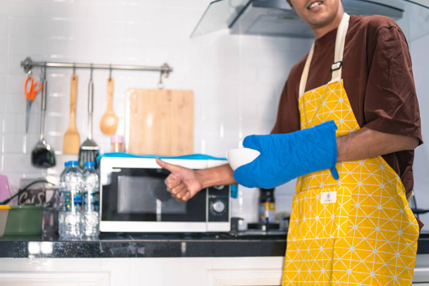 homem desfocado asiático cozinhar na cozinha de casa Ele mantém tigela e espátula para grande mão no microondas na cozinha desfocado fundo - Foto, Imagem