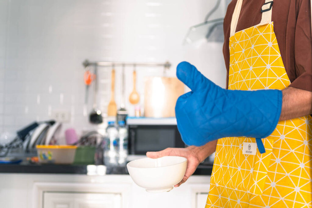 wazig man aziatische koken in keuken van huis hij houdt kom en spatel aan grote hand op magnetron in keuken wazig achtergrond - Foto, afbeelding