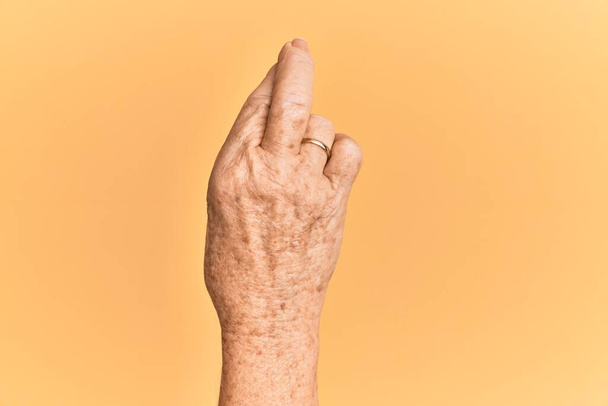 Senior kaukázusi kéz sárga elszigetelt háttér gesztikuláló ujjak keresztbe, babona és szerencsés gesztus, szerencsés és remény kifejezés  - Fotó, kép
