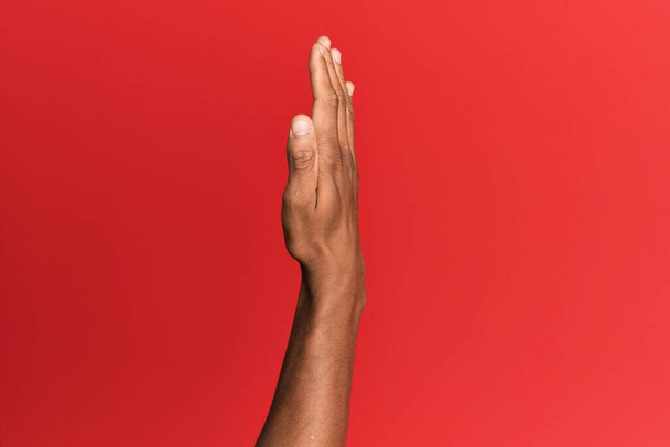 Ruka hispánského muže nad červeným izolovaným pozadím ukazující stranu natažené ruky, jak tlačí a dělá gesto stop  - Fotografie, Obrázek