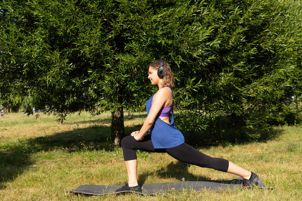 Female fitness instructor does, shows exercises in a green park. Sport concept. - Foto, imagen