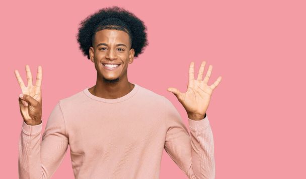 Uomo afro-americano con i capelli afro indossa abiti casual mostrando e indicando con le dita il numero otto, sorridendo fiducioso e felice.  - Foto, immagini