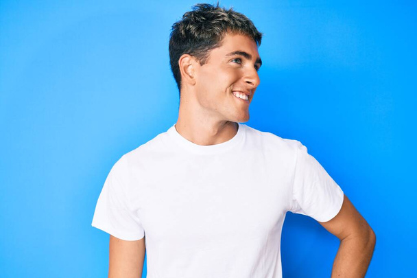Young handsome man wearing casual white t shirt looking away to side with smile on face, natural expression. laughing confident.  - Photo, Image