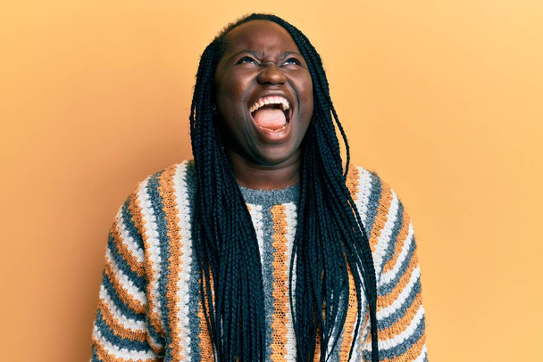 Young black woman with braids wearing casual winter sweater angry and mad screaming frustrated and furious, shouting with anger. rage and aggressive concept.  - Photo, Image