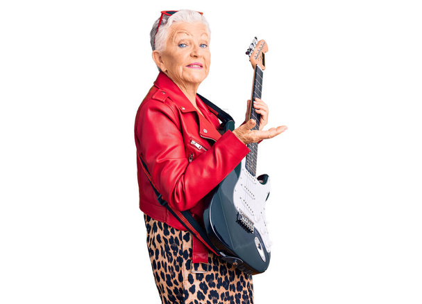 Senior beautiful woman with blue eyes and grey hair wearing a modern look playing electric guitar pointing aside with hands open palms showing copy space, presenting advertisement smiling excited happy  - Fotoğraf, Görsel