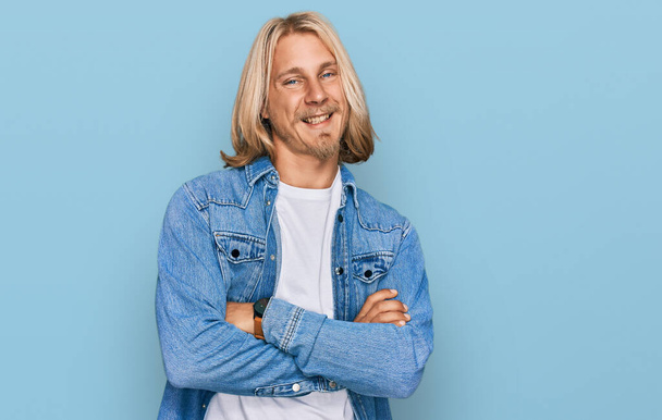 Caucasian man with blond long hair wearing casual denim jacket happy face smiling with crossed arms looking at the camera. positive person.  - Photo, Image