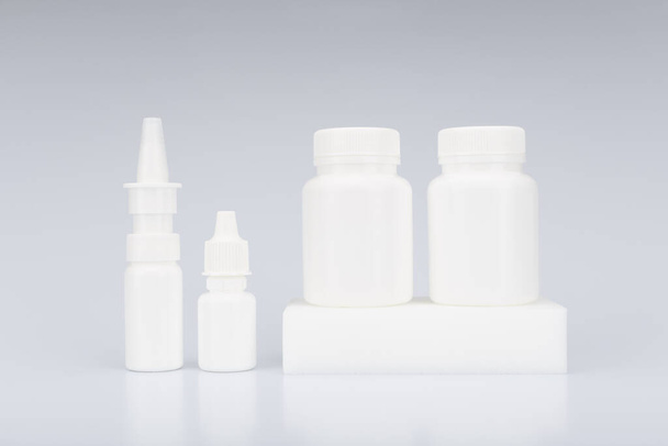 Nose spray, eye drops and two medication bottles on podium against light grey background. Concept of medical treatment - Foto, Imagem