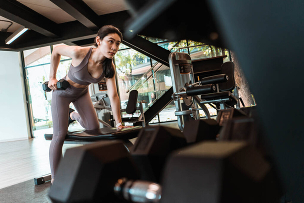 Молодая красивая стройная женщина делает упражнения с гантелями в тренажерном зале - Фото, изображение