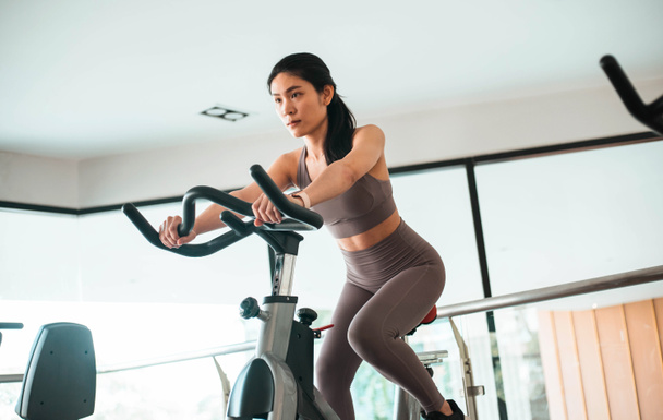 Belle jeune femme asiatique faisant du cardio sur un vélo d'appartement à la salle de gym - Photo, image