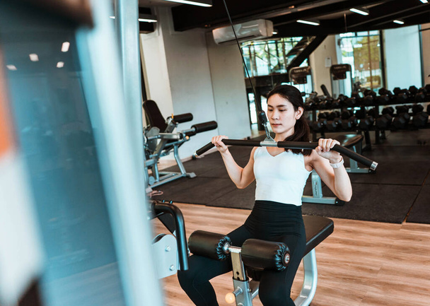 Jeune belle femme en tenue de sport travaillant avec une machine dans la salle de gym - Photo, image