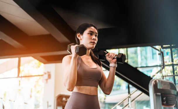 Young beautiful slim woman doing exercises with dumbbell in gym - Photo, Image