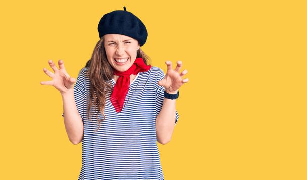 Jonge mooie blonde vrouw dragen franse baret en gestreepte t-shirt lachen grappig doen klauw gebaar als kat, agressieve en sexy uitdrukking  - Foto, afbeelding