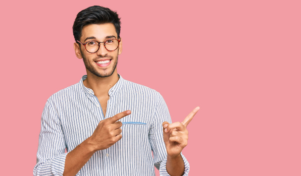 Young handsome man wearing casual clothes and glasses smiling and looking at the camera pointing with two hands and fingers to the side.  - Photo, Image