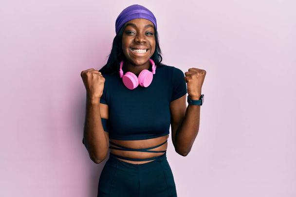 Молодая африканская американка, одетая в спортивную одежду и пользующаяся наушниками, удивлена и поражена успехом с поднятыми руками и открытыми глазами. победитель концепция.  - Фото, изображение