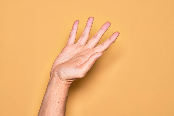 Χέρι καυκάσιου νέου άνδρα που δείχνει τα δάχτυλά του πάνω από απομονωμένο κίτρινο φόντο παρουσιάζοντας με ανοιχτή παλάμη, φτάνοντας για υποστήριξη και βοήθεια, χειρονομία βοήθειας - Φωτογραφία, εικόνα