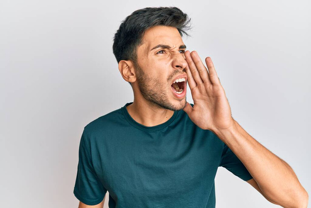 Jonge knappe man draagt nonchalante kleren schreeuwend en schreeuwend naast elkaar met hand op mond. communicatieconcept.  - Foto, afbeelding