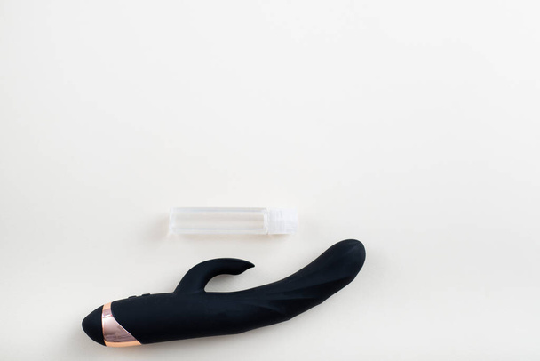 Black vaginal clitoral dildo and a jar of lubricant on a white background. Masturbation kit and blank space for text - Foto, Bild