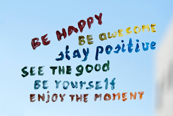 Positive Phrasen in verschiedenen Farben auf einem Fensterglas vor blauem Himmel geschrieben - Foto, Bild