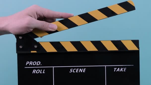 Movie clapperboard. Close up man hand hold empty black and yellow stripe film making movie slate isolated on blue green background studio. Clapped on and off. film slate for video production. - Footage, Video
