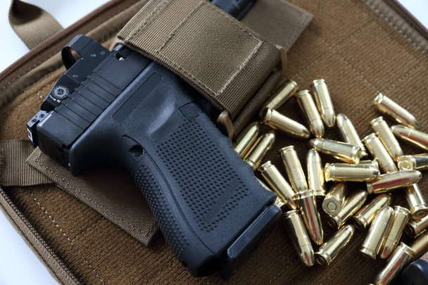 Closeup of a 9 mm pistol with red dot sight on a soft case with bullets.   - Photo, Image
