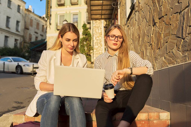 Two young smiling women looking at laptop monitor, sitting outdoors - Foto, Imagem