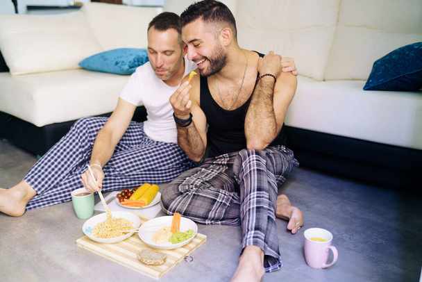 gay pareja comer juntos sentado en su sala de estar piso. - Foto, imagen