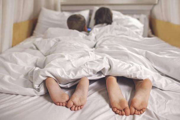 Kaksi sisarusta katsomassa videota mobiili elektroninen laite sängyssä, gadget riippuvuus, elämäntapa - Valokuva, kuva