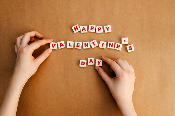 Manos humanas organizando texto feliz día de San Valentín sobre fondo de papel kraft. - Foto, imagen
