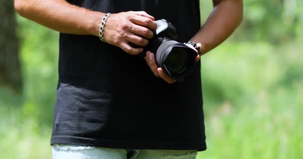 Man photographer with a photo camera configures outdoor - Πλάνα, βίντεο