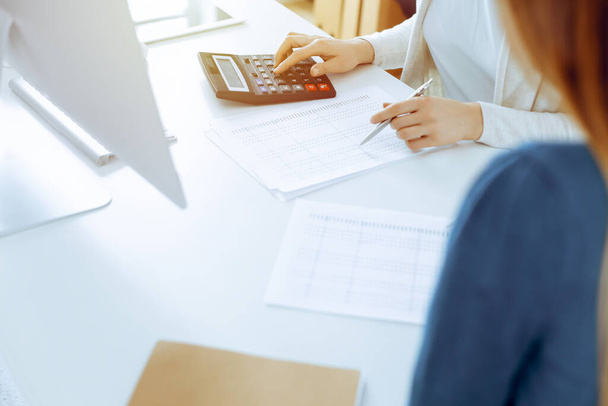 Accountant checking financial statement or counting by calculator income for tax form, hands close-up. Business woman sitting and working with colleague at the desk in office. Audit concept - Valokuva, kuva