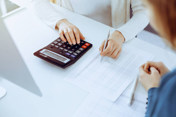 Accountant checking financial statement or counting by calculator income for tax form, hands close-up. Business woman sitting and working with colleague at the desk in office. Audit concept - Fotó, kép