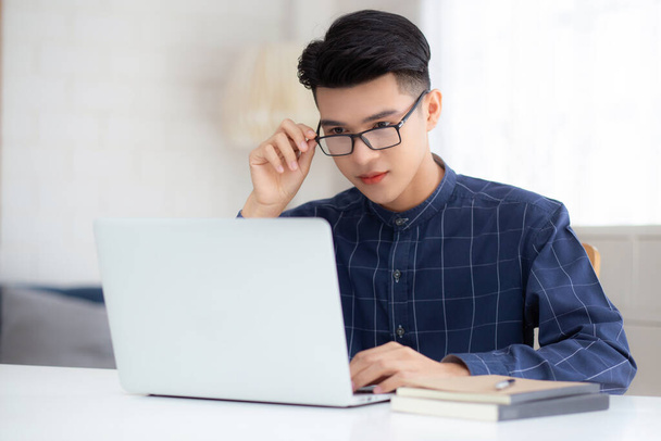 Молодой бизнесмен в очках работает из дома с ноутбуком на столе, внештатный мужчина сидит дома, используя ноутбук для связи на столе, предприниматель в стартап-бизнесе, новая нормальная. - Фото, изображение