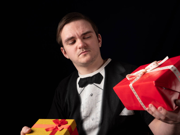 young guy in a black t-shirt suit chooses gifts on a black background - Photo, Image