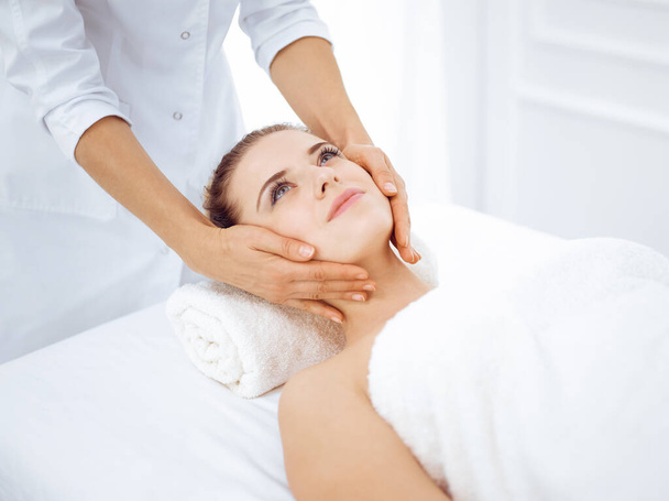 Young and blonde woman enjoying facial massage in spa salon. Beauty concept - Foto, immagini