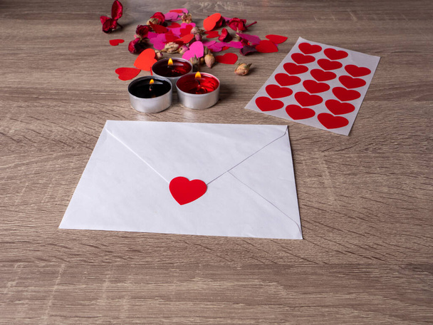 white envelope next to candles with red rose petals and hearts on the table - Photo, Image