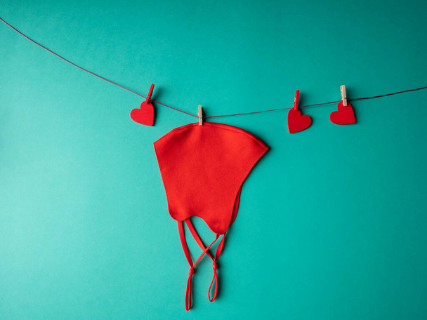 Red mask that weighs on a rope with three red hearts that are fixed with clothespins on a green background - Fotografie, Obrázek