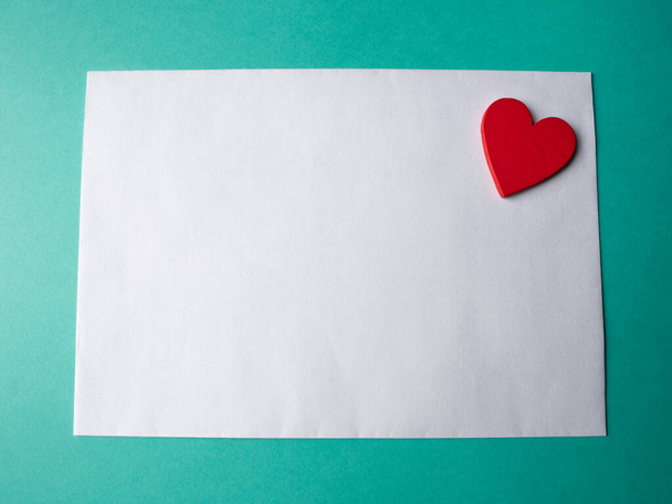 White paper and a red hearth on a green background. A template for your project for valentine's day - Photo, Image