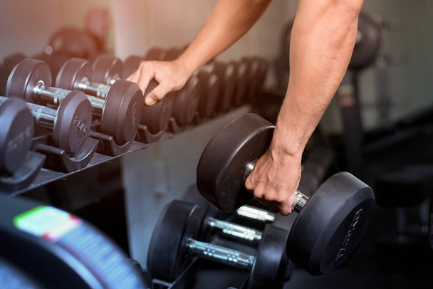 Muscular fitness man bodybuilder is workout with dumbbells in gym - Fotografie, Obrázek