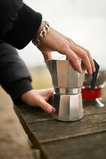 Reisender Mann, der im Freien mit einer metallenen Geysir-Kaffeemaschine auf einem Gasbrenner Kaffee macht, Schritt für Schritt. Reiseaktivitäten für Entspannung, Buschboot, Abenteuer, Reisen, Tourismus und Campingkonzept - Foto, Bild