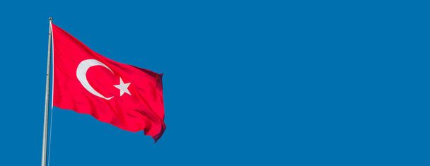 Banner με κόκκινη τουρκική εθνική σημαία που κρατά λευκό μισοφέγγαρο και αστέρι στη σημαία στο γαλάζιο του ουρανού και αντίγραφο χώρο για κείμενο - Φωτογραφία, εικόνα