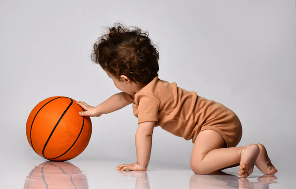 Baby boy dressed in a bodysuit with interest plays a basketball on a gray background. - Fotoğraf, Görsel