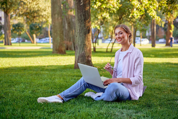 Bizneswoman siedzi trawiasty letni park za pomocą laptopa Biznes osoba pracująca zdalnie. Outdoor Successful european kaukaski kobieta freelancer zrobić wideo zadzwoń nauczyciel nauka praca online lekcje  - Zdjęcie, obraz