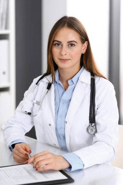 Doctor woman filling up medical form while sitting at the desk in hospital office. Physician at work. Medicine and health care concept - Foto, imagen