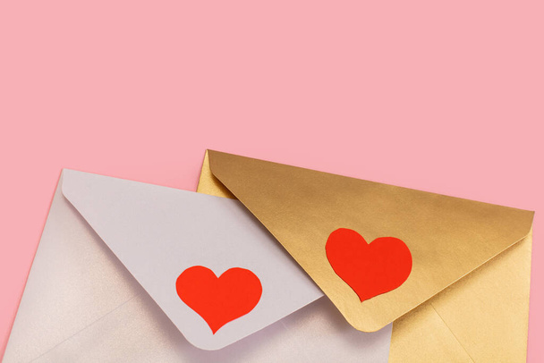 light mother-of-pearl and golden paper envelopes with red hearts isolated on pink background - Photo, image